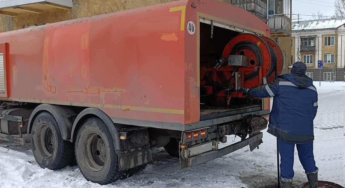 Каналопромывочная машина и работник прочищают засор в канализационной системе в Холмске
